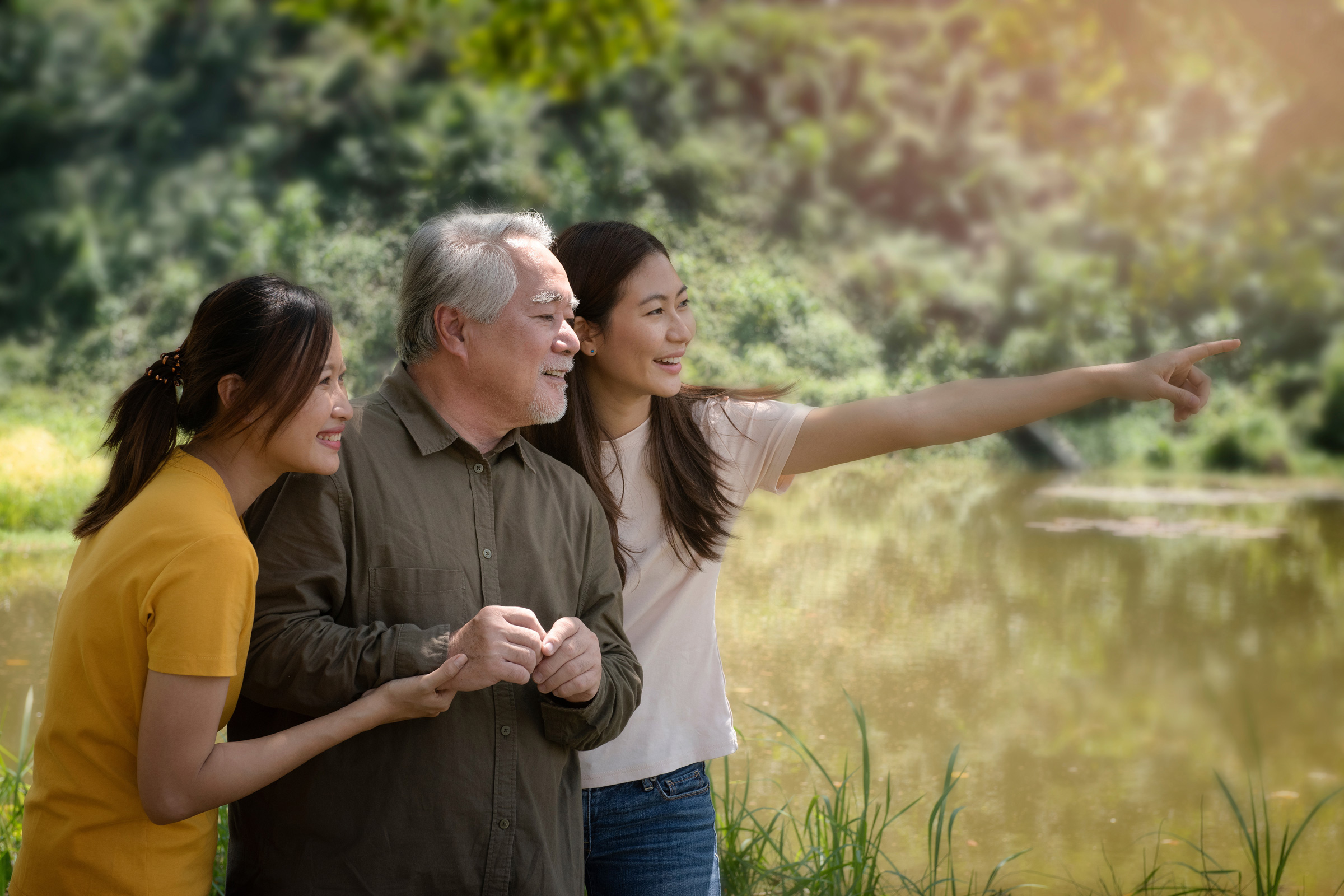 A joyful family moment by the water, featuring two women and an older man enjoying nature and pointing at something.