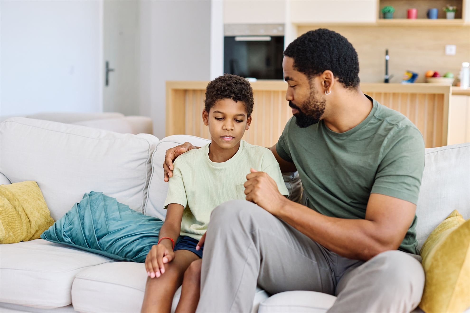 Father and son having a heartfelt conversation while sitting on a couch in a modern living room.