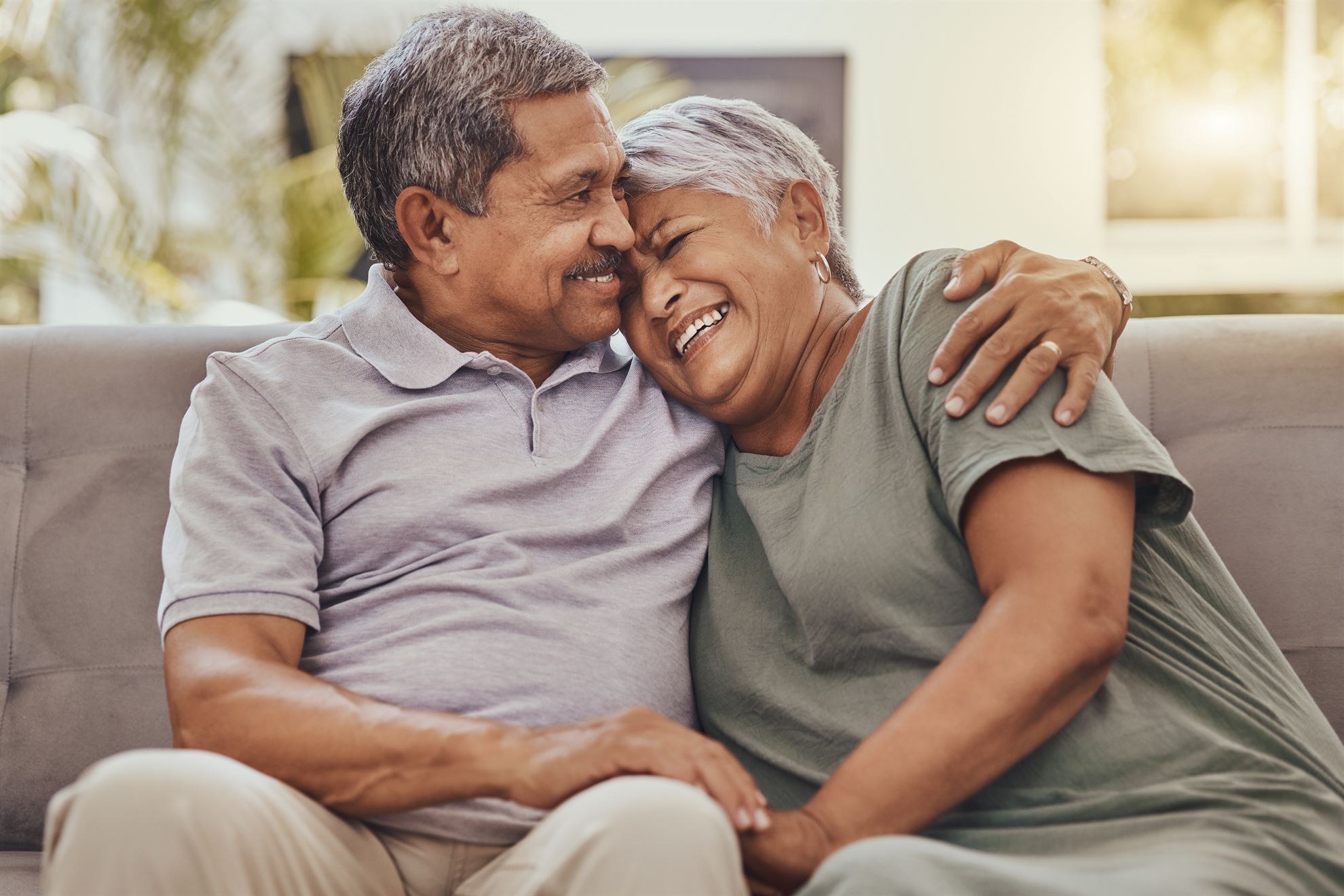 Happy senior couple sharing a joyful moment together on a couch, embracing and smiling at each other.
