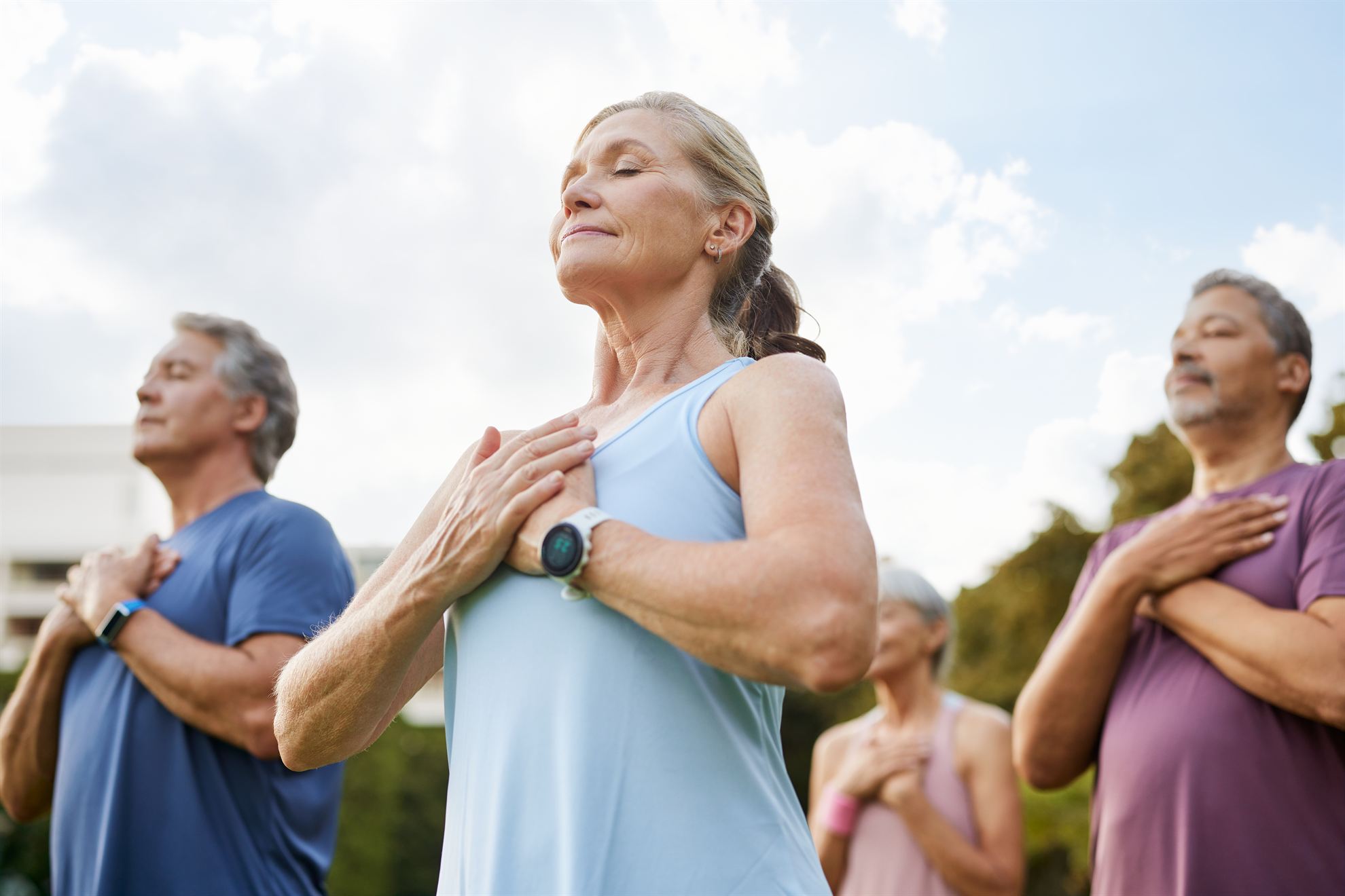 Group of adults practicing mindfulness and deep breathing outdoors, promoting wellness and relaxation.