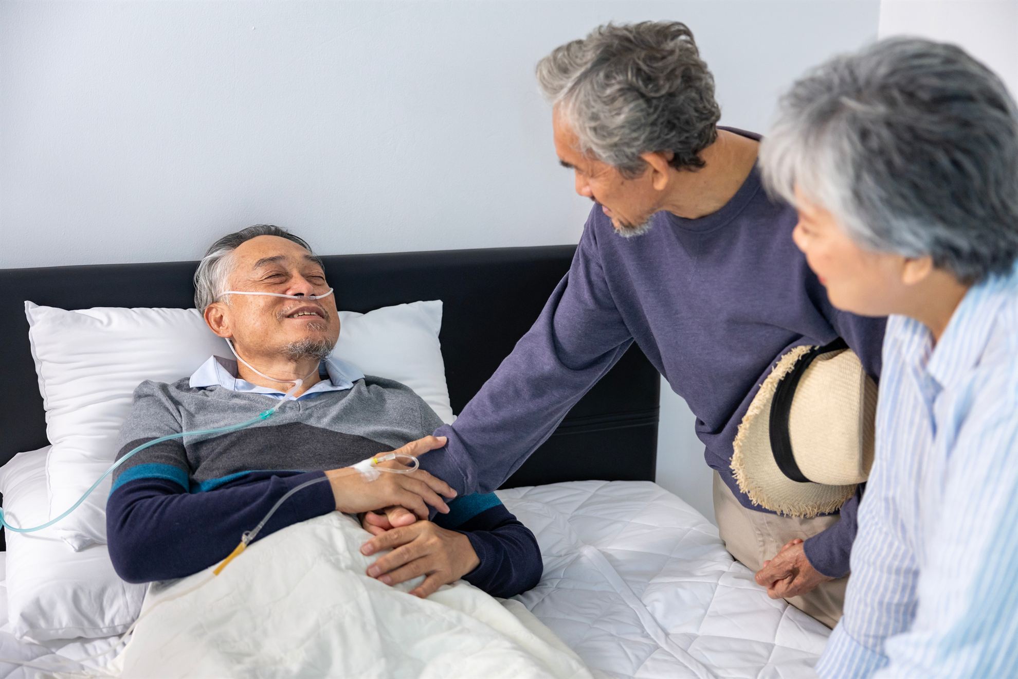 Elderly man in bed receiving care from two loved ones, showcasing a moment of compassion and support in a home setting.