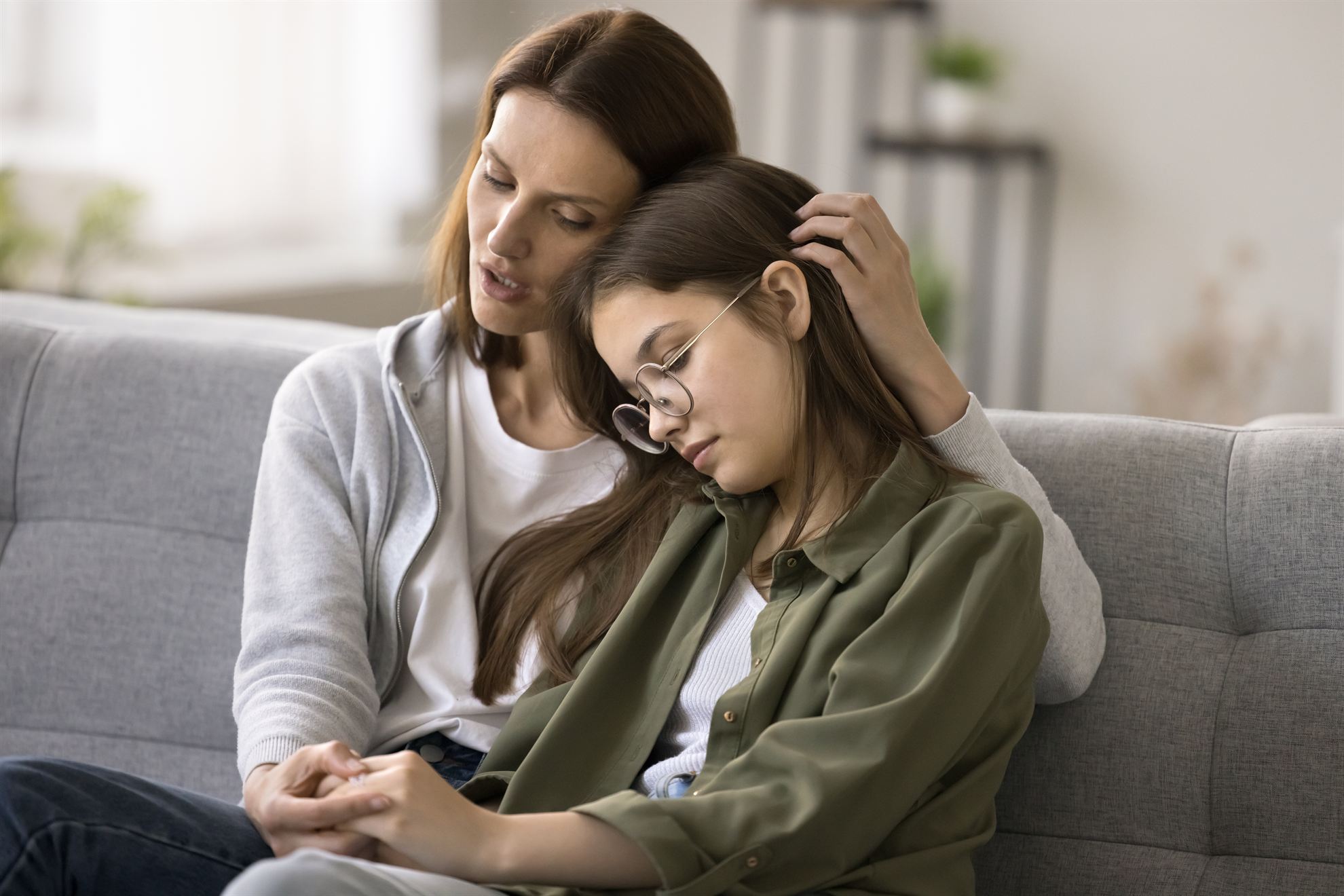 A mother comforting her daughter while sitting on a couch in a cozy living room setting.