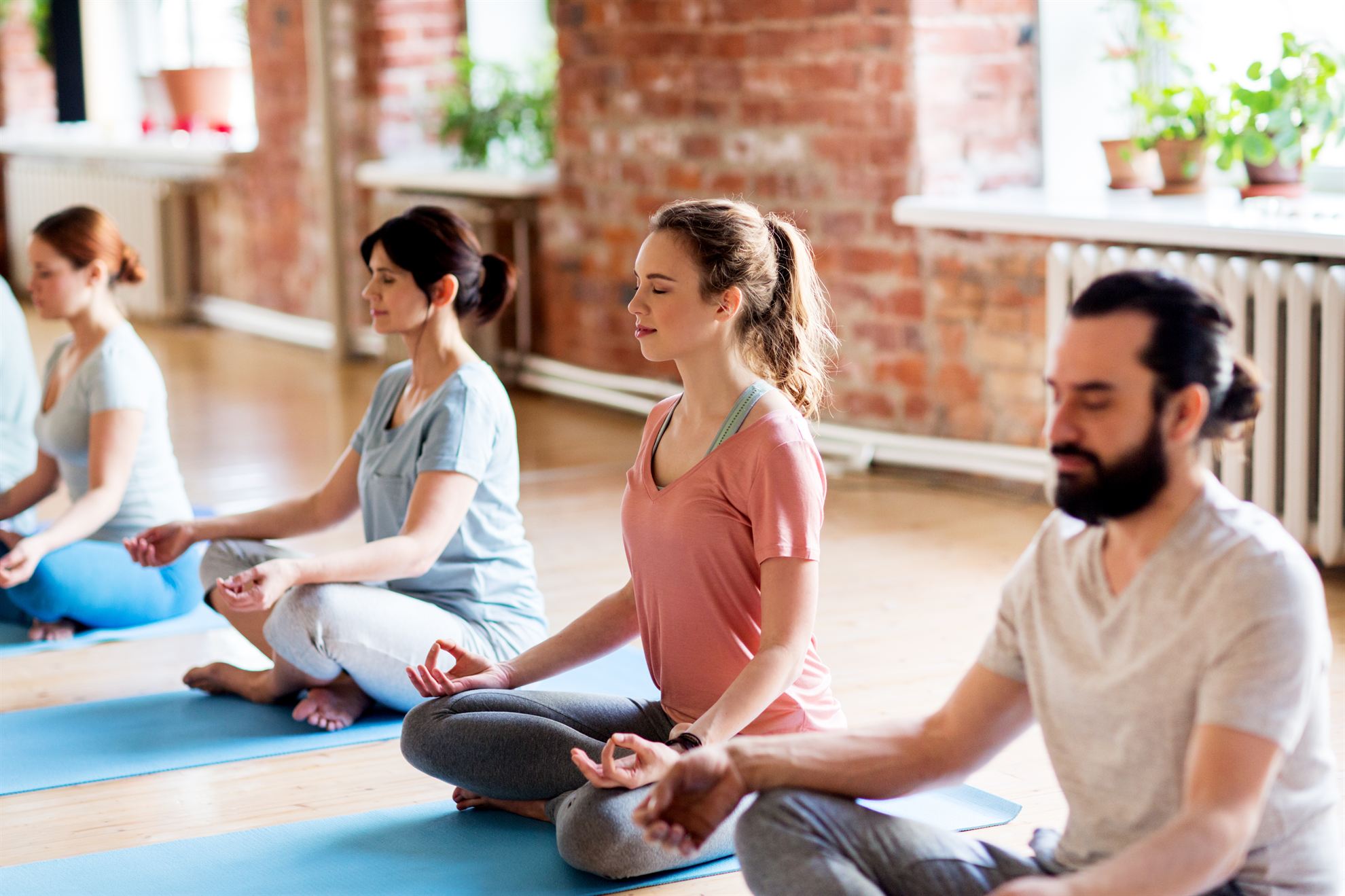 Group of people practicing yoga and meditation in a bright, serene studio with brick walls and plants.