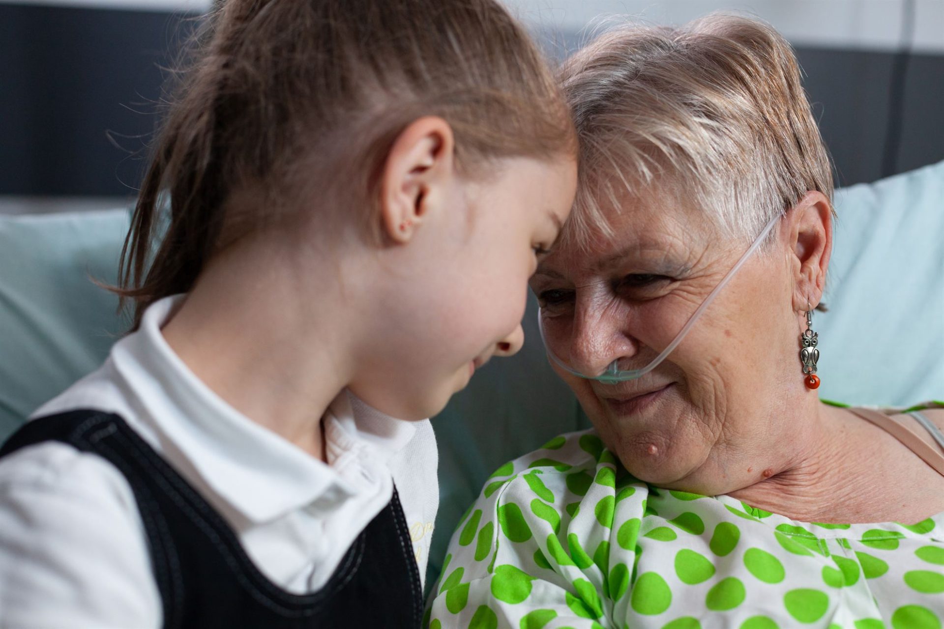 A girl and an elderly woman share a tender moment, smiling at each other in a hospital setting.