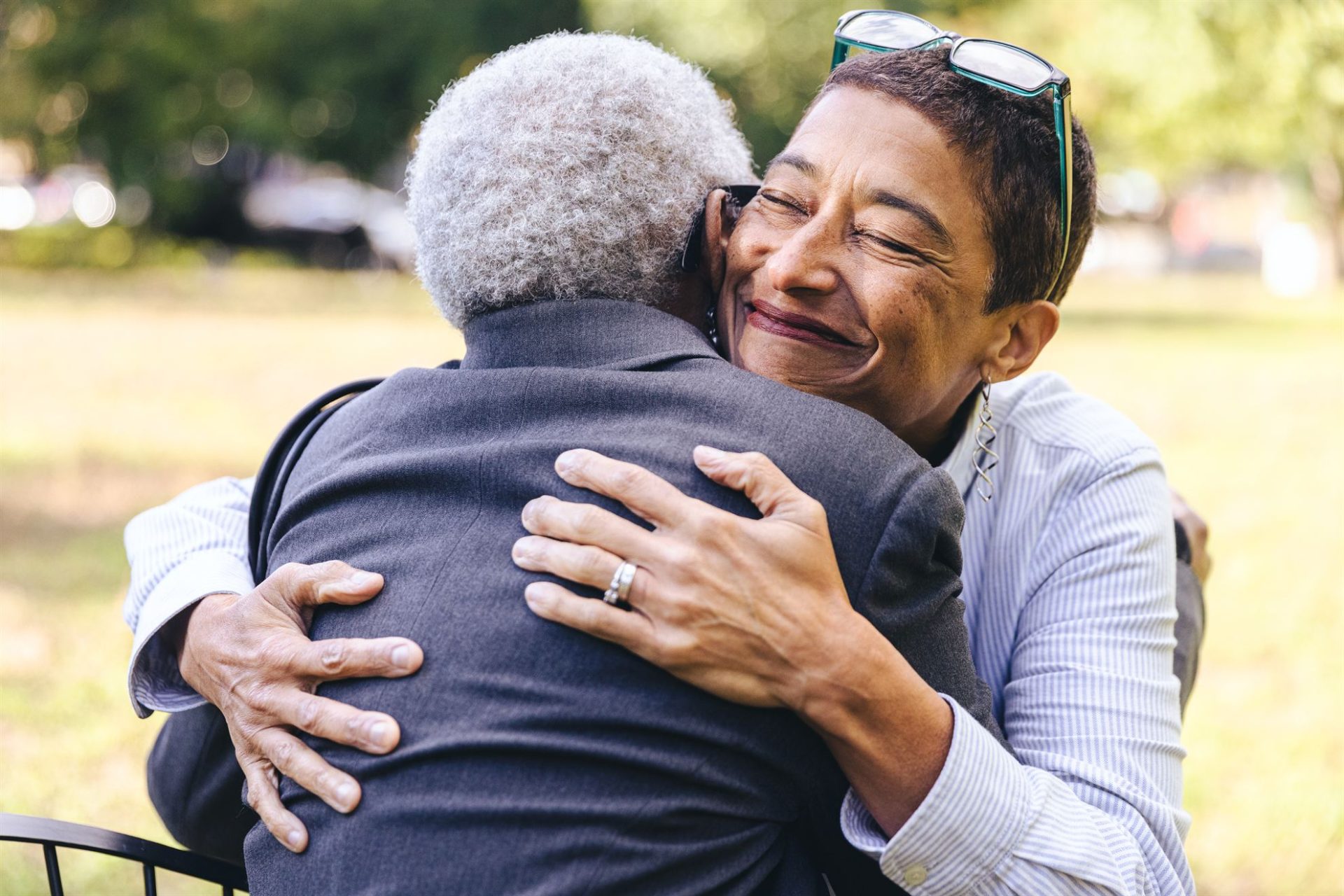 Two people embrace warmly in a park, smiling and expressing joy in their connection.